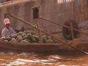 A man in a small boat buys a huge order of fruit from a larger boat.